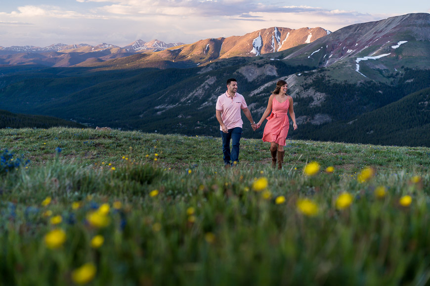 A couple walking on a grassy hill with mountains in the background.
