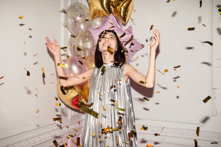 A woman in a silver dress is surrounded by balloons and confetti.