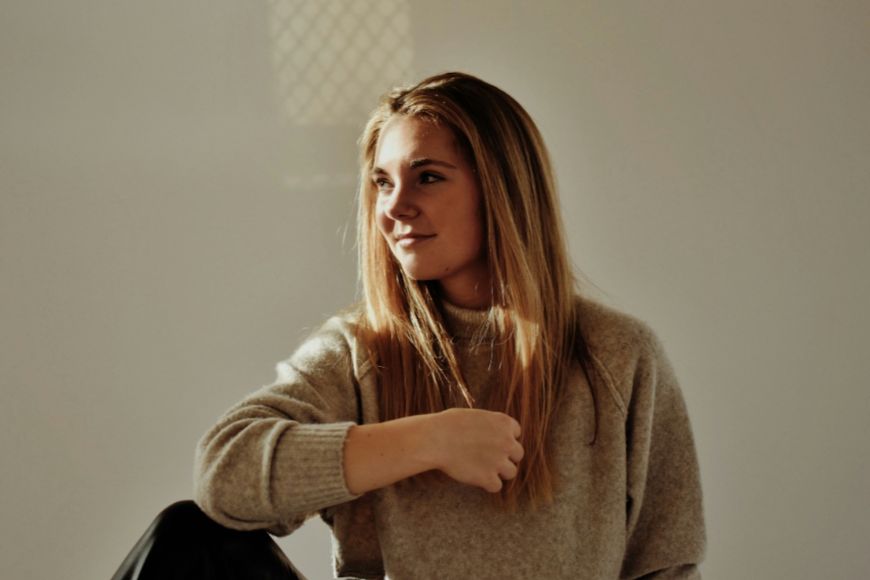 A young woman in a beige sweater sitting on a chair.