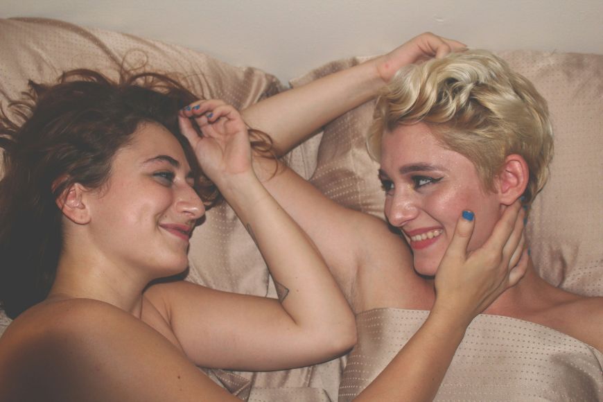 Two women laying on a bed and smiling at each other.