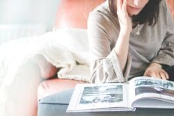 A woman is sitting on a couch reading a photo book.