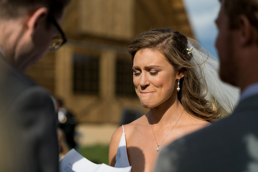 A bride smiles as she reads her vows in front of a barn.