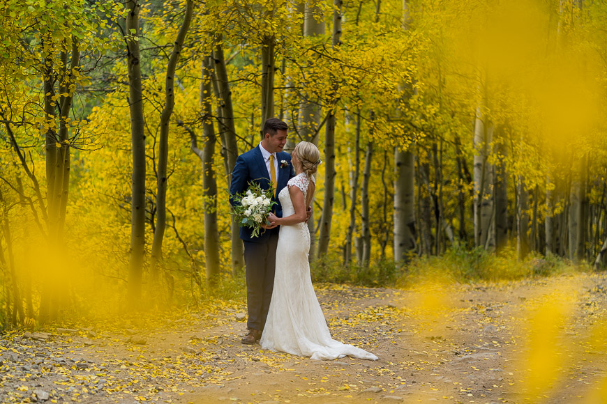 A bride and groom standing in a yellow forest.