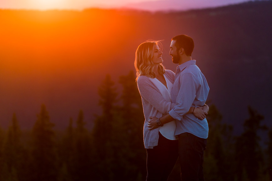 A couple embraces in front of a sunset in the mountains.
