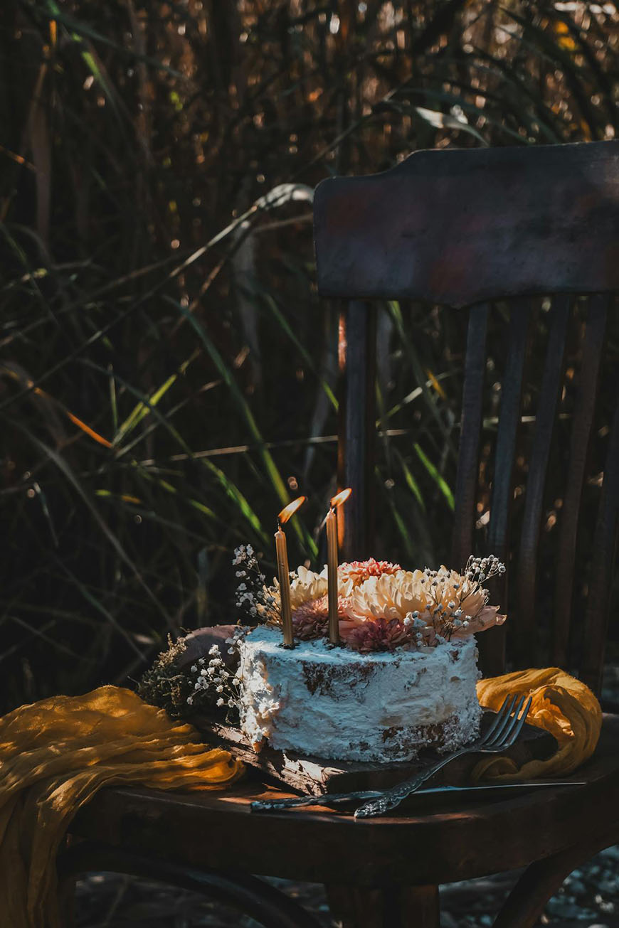 A cake sits on a wooden chair in a field.