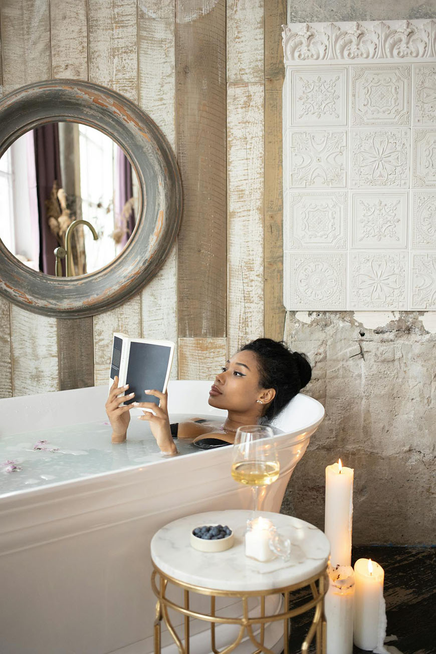 A woman is sitting in a bathtub reading a book.