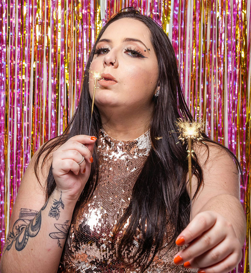 A woman holding a sparkler in front of a pink backdrop.