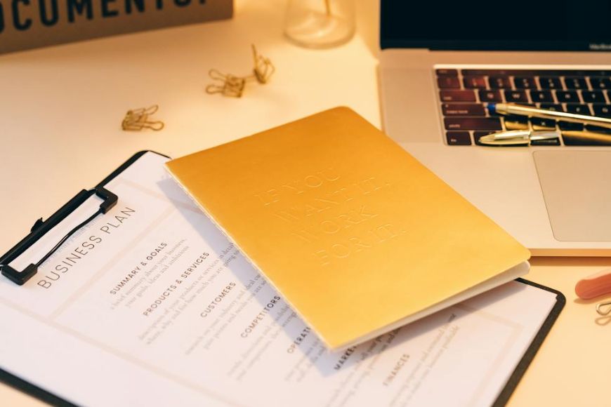 A gold notebook on a desk next to a laptop.