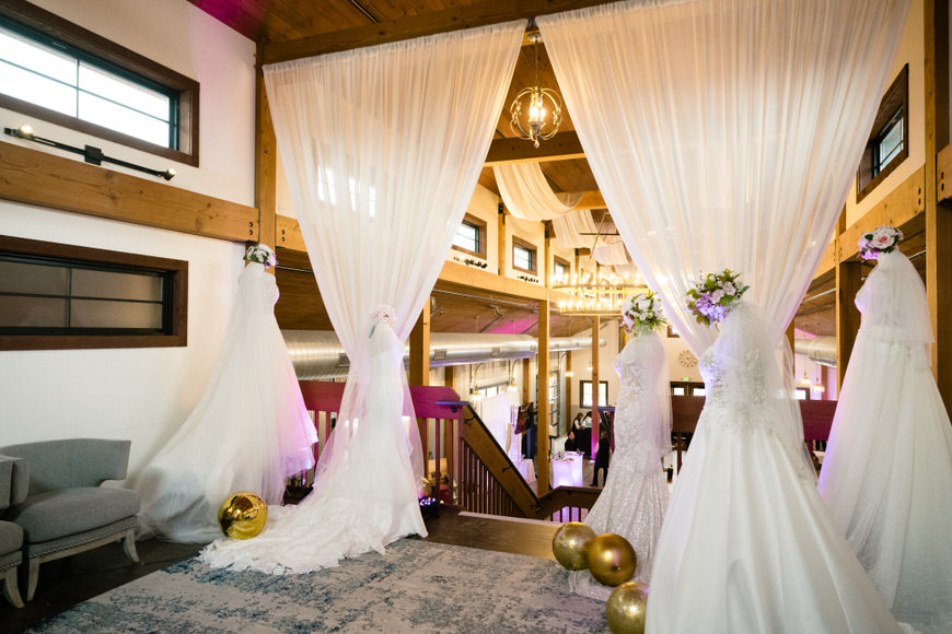Wedding dresses hang in a room with a chandelier.