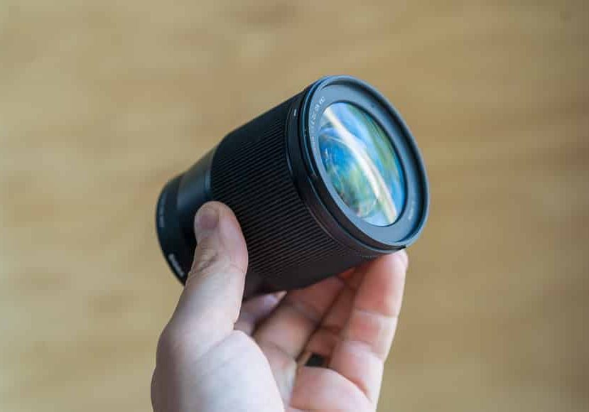 A person holding up a black lens on a wooden background.