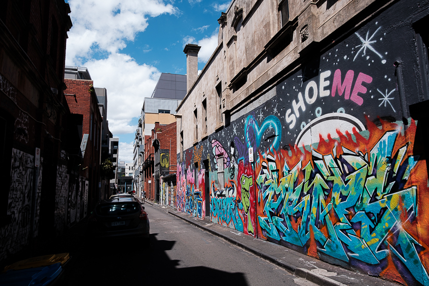 An urban alleyway decorated with vibrant graffiti art, under a partly cloudy sky.