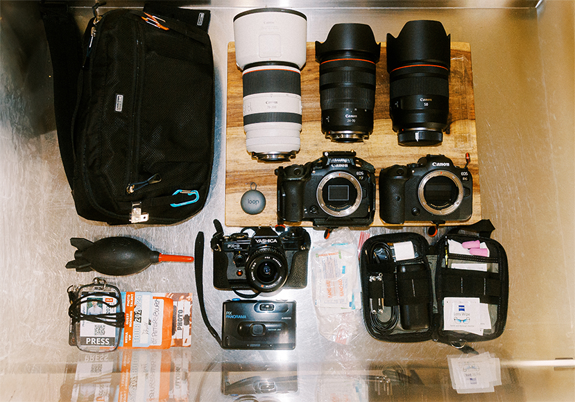 A collection of professional photography equipment laid out on a wooden surface, including cameras, lenses, and accessories.