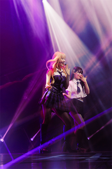 Two singers performing on stage amidst colorful lighting.