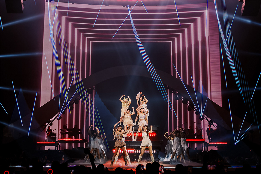 A dynamic stage performance with dancers in elaborate costumes under vibrant laser lights.