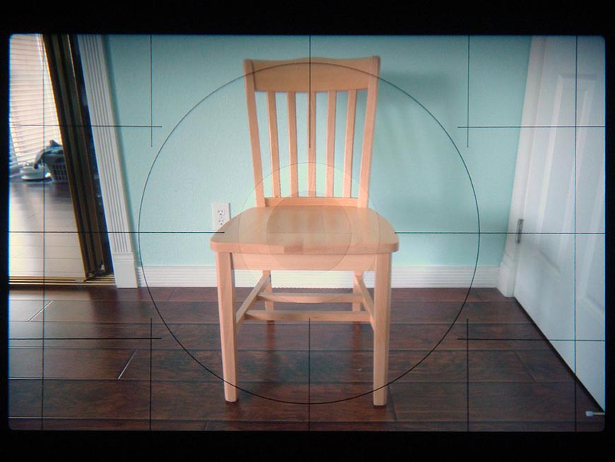 Wooden chair centered in viewfinder crosshairs on a tiled floor.
