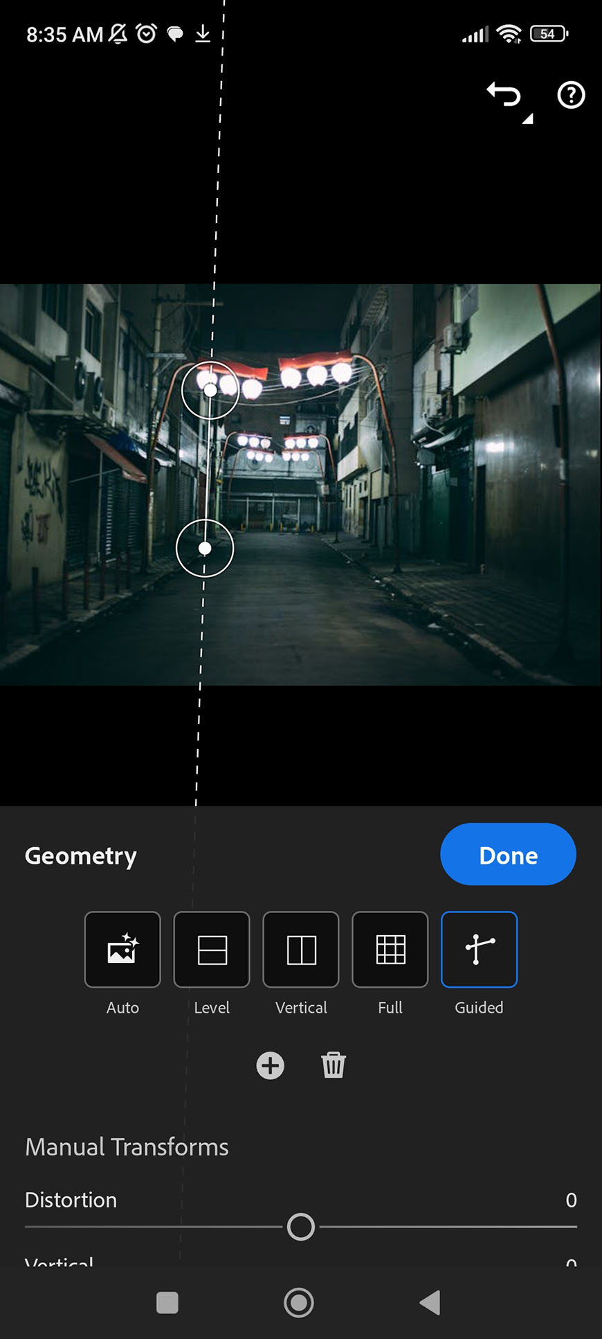 A screenshot of a smartphone editing interface adjusting the geometry of a nighttime photo of an alleyway.