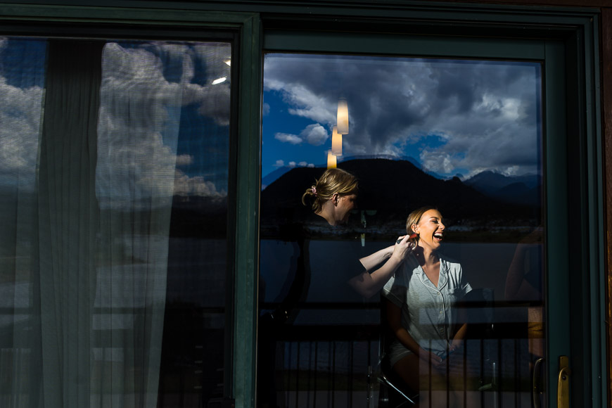 Woman laughing inside a room, reflected in a glass door against a backdrop of mountains and clouds.