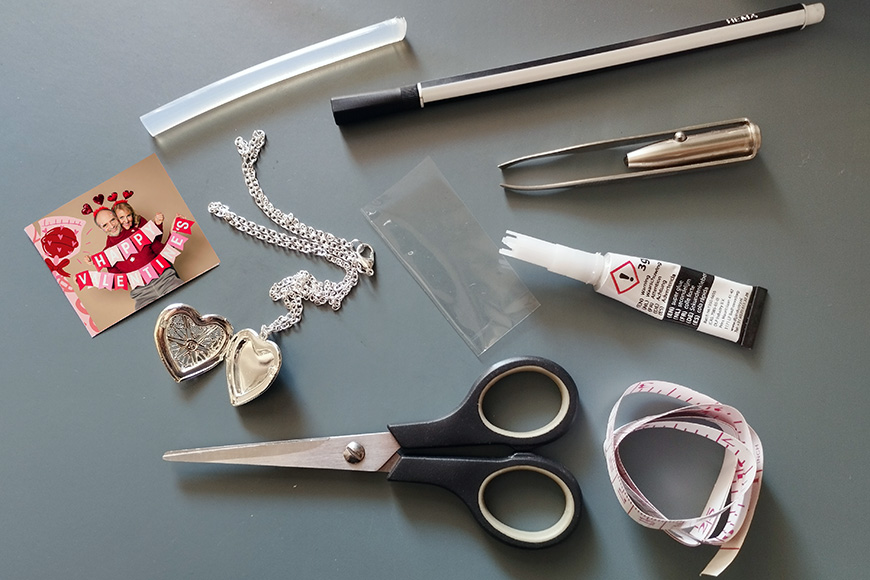 Assorted items including scissors, pen, tube of glue, chain necklace, and measuring tape on a gray surface.
