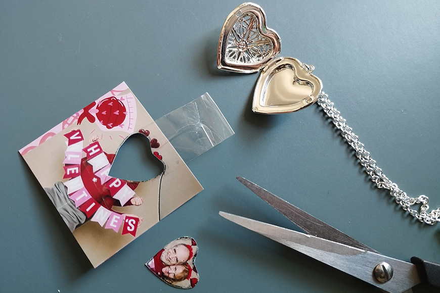 A valentine's day card with a heart cut out, a pair of scissors, and a heart-shaped locket on a chain.