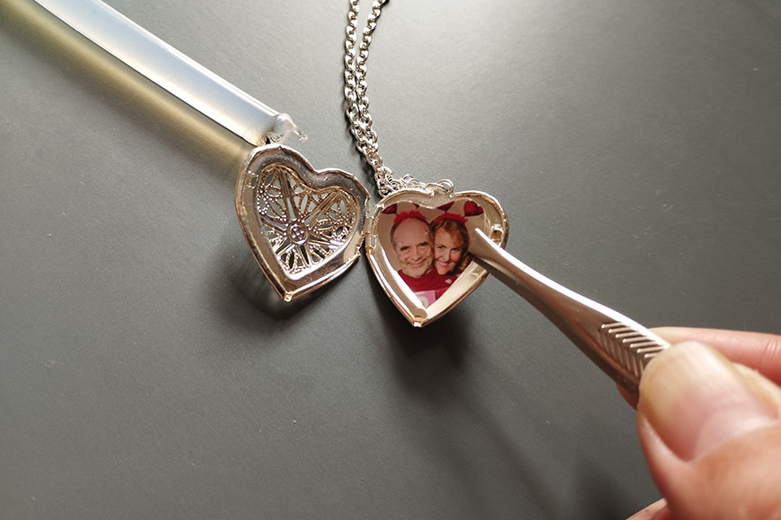 A hand holding a heart-shaped locket with a photo inside, next to a key-shaped pendant, both resting on a dark surface.
