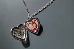 A locket necklace with a heart shape containing a photo of a smiling couple, open to reveal another heart design inside.