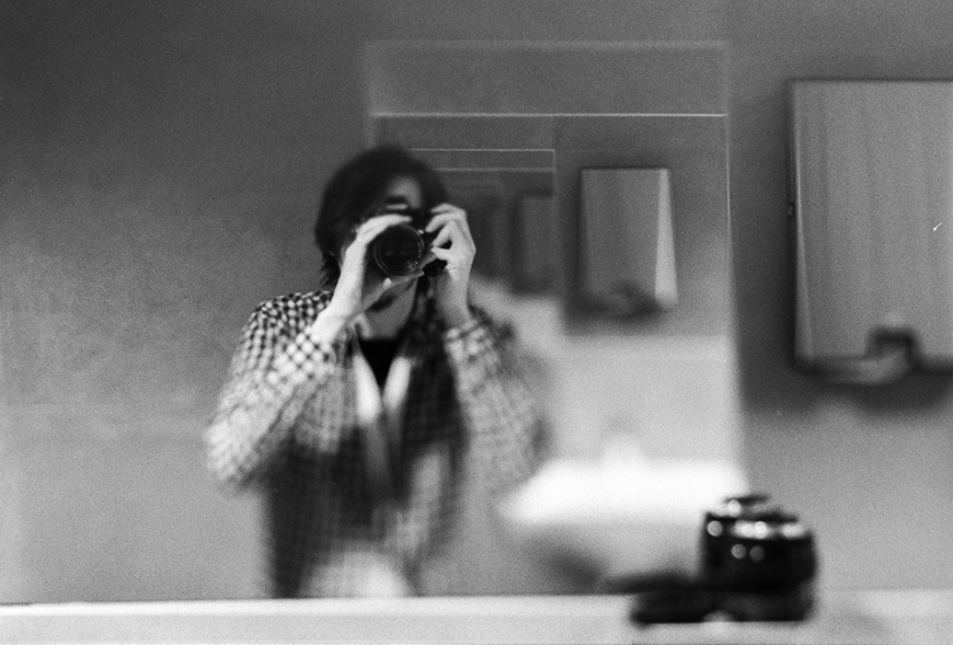 Person taking a photograph of their reflection in a bathroom mirror.