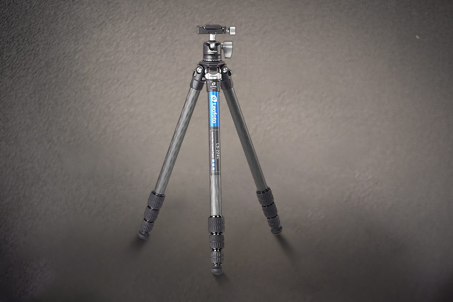 A camera tripod with extended legs on a textured gray background.