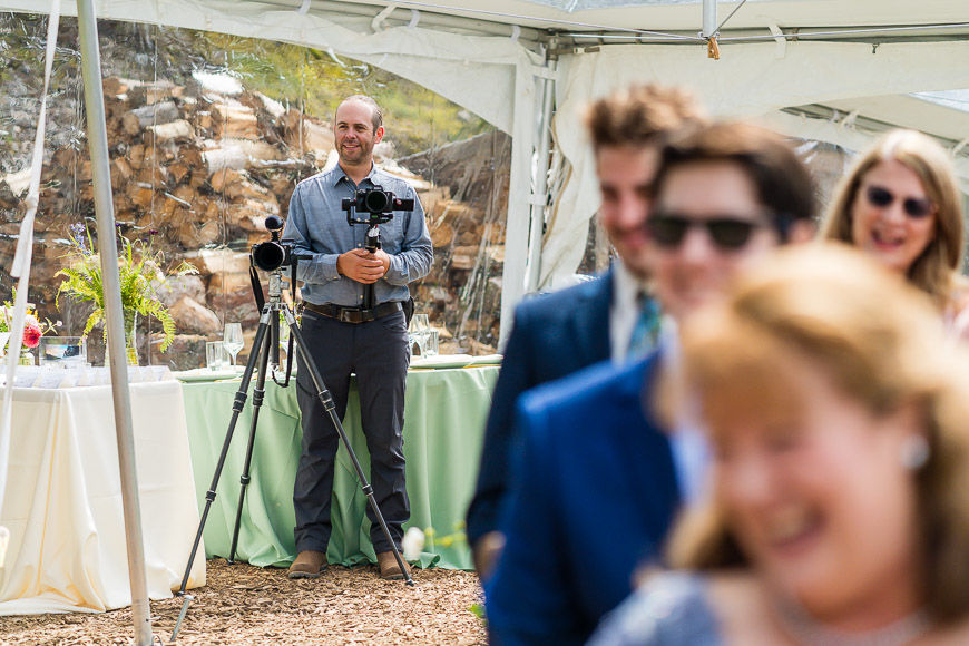 Videographer recording a joyful outdoor event with attentive guests in the foreground.