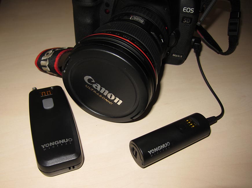 A canon dslr camera with a lens attached, alongside two yongnuo wireless flash triggers on a table.