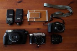 Assorted photography equipment on a wooden surface, including cameras, lenses, and flash units.