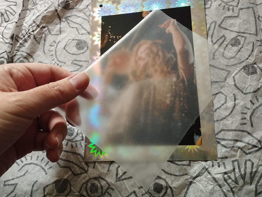 A person's hand holding a holographic photograph over a patterned background.