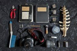 Assortment of personal items laid out on a textured surface, including a camera, notebooks, headphones, and various accessories.