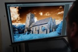 A person observing an infrared photograph of a church displayed on a computer monitor.