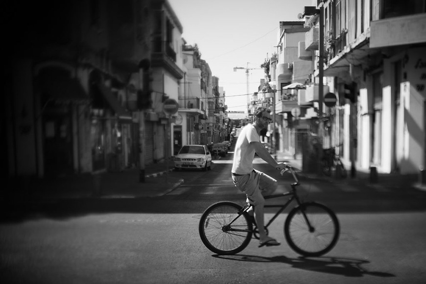 Person riding a bicycle down a quiet street in a black and white photograph.