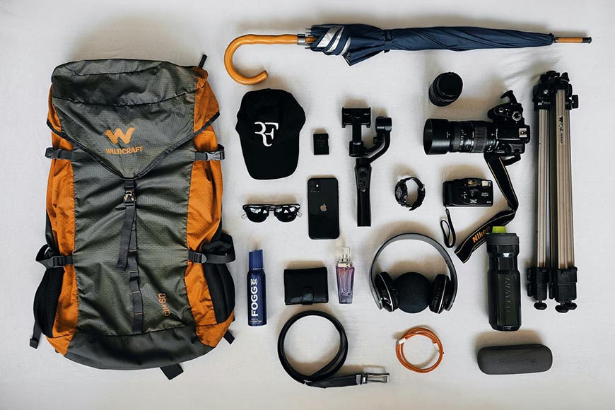 Traveler's gear laid out, including a backpack, camera equipment, walking stick, hat, sunglasses, and other accessories.