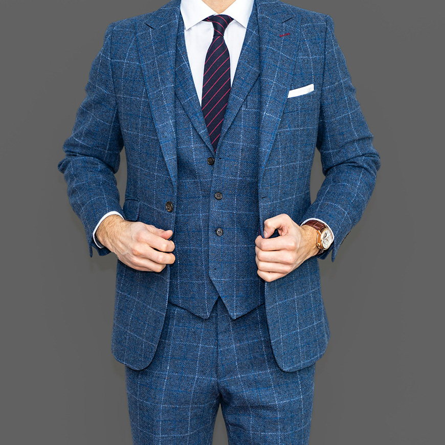 A person wearing a blue checkered three-piece suit and a striped tie, adjusting their suit jacket.