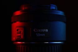 A canon 50mm lens illuminated by red and blue lighting against a dark background.