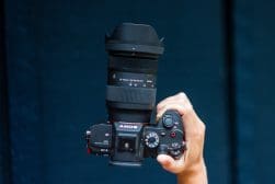 A hand holding a camera with a zoom lens against a dark blue background.
