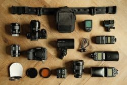 Photography equipment neatly arranged on a wooden surface, including cameras, lenses, a flash, and various accessories.