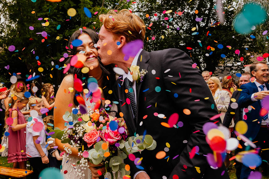 A joyful couple being showered with colorful confetti at a wedding celebration.