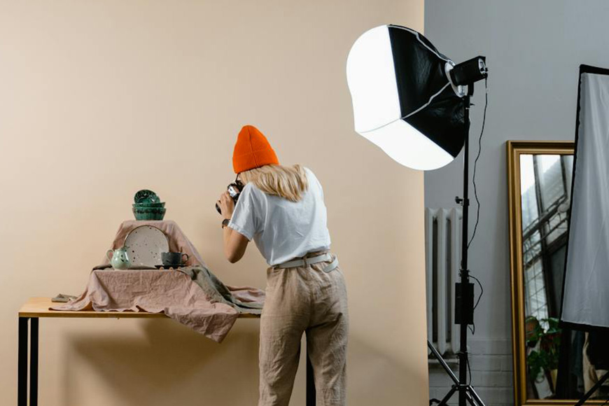 Photographer capturing images of ceramic pottery in a well-lit studio setup.