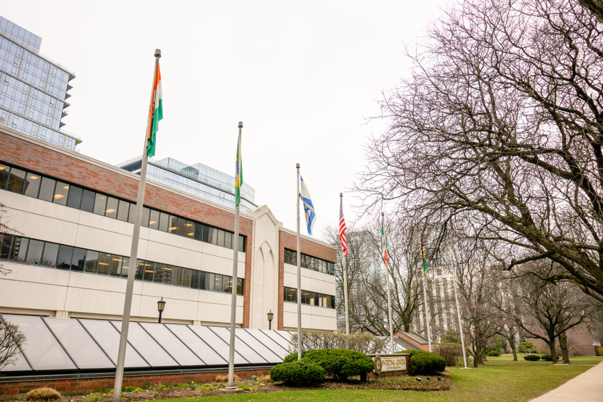 Flags in front of a modern building with bare trees nearby.
