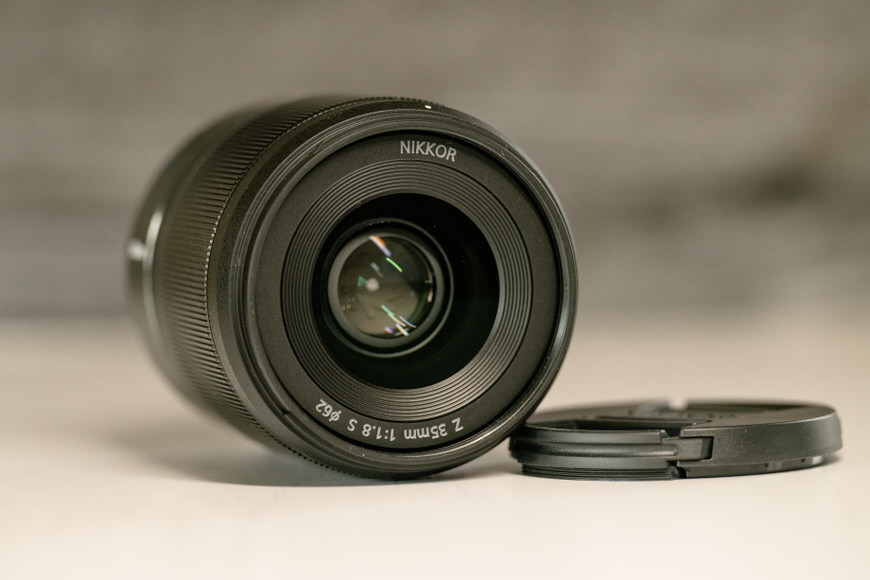 A nikkor camera lens placed on a surface with its lens cap off to the side.