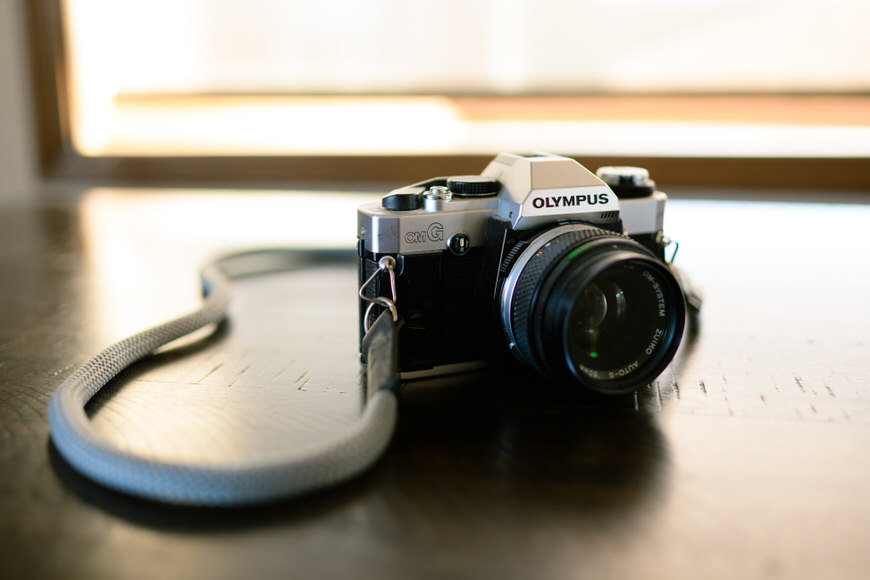 An olympus film camera with a strap resting on a wooden surface.