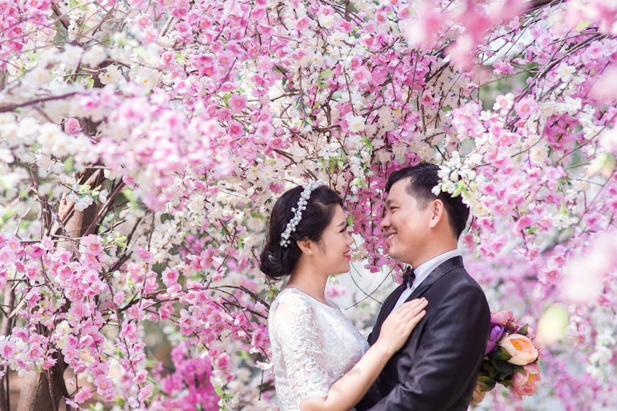 A couple in wedding attire sharing a moment surrounded by blooming cherry blossoms.