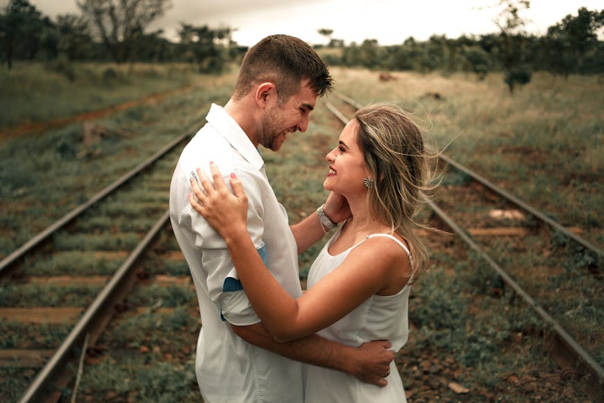 A couple embracing and smiling at each other on a railway track with grass and trees in the background.