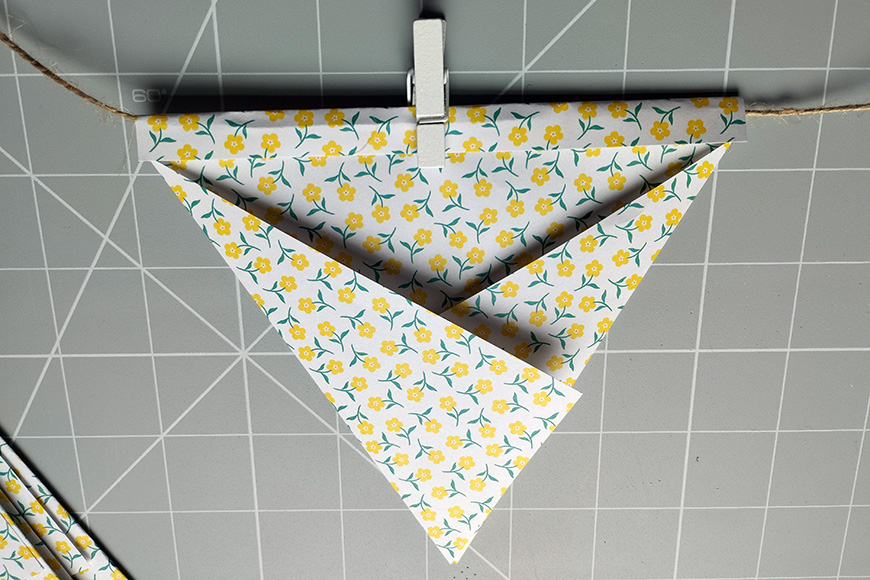 A patterned paper origami bird suspended from a string against a tiled background.