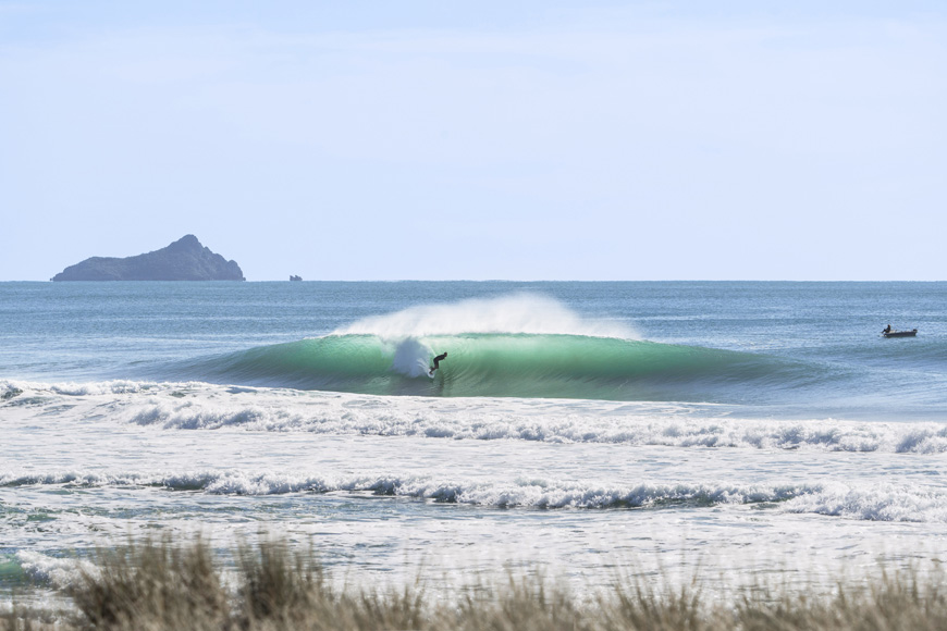 A surfer riding a green wave with an island in the background.