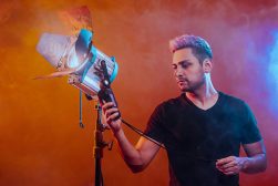 Man adjusting a studio light against a smoky, colored background.