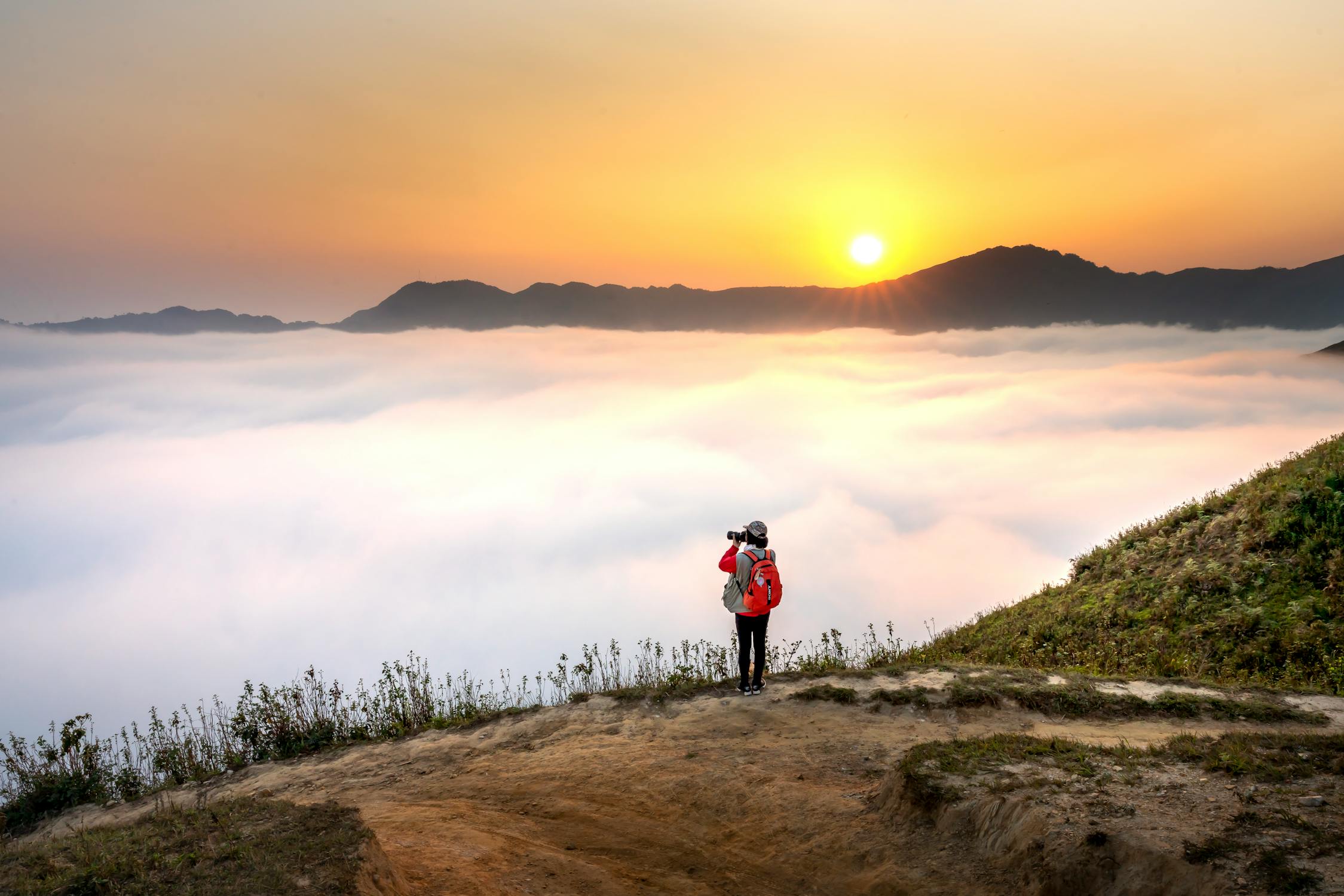 Photographer capturing the sunrise above a sea of clouds on a mountain.